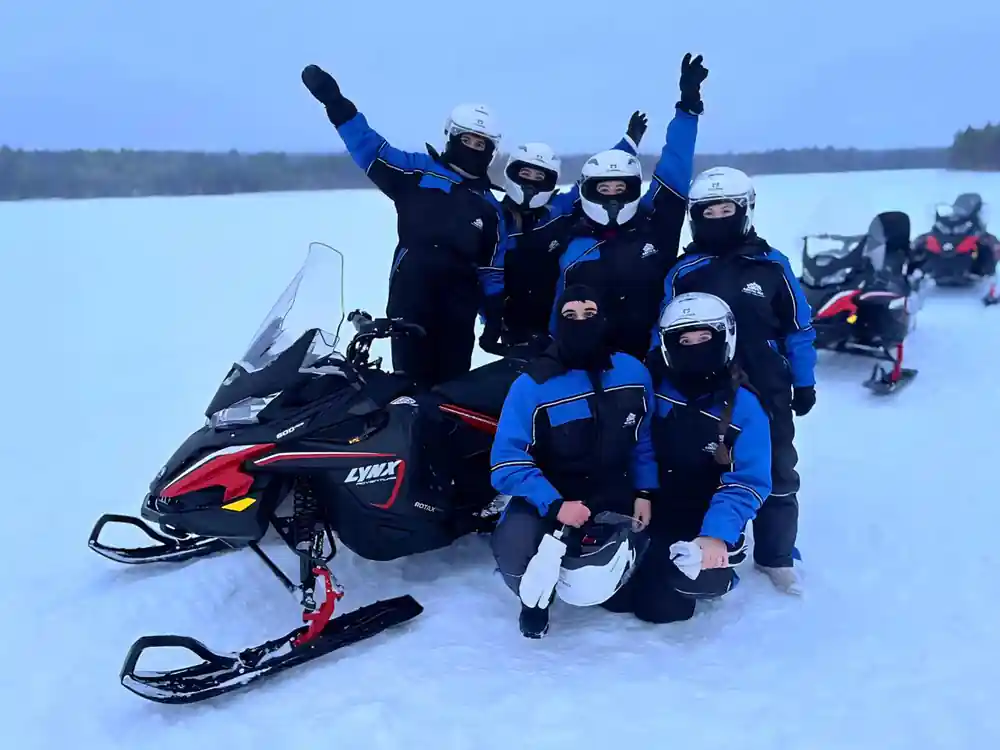 Group of five people posing with snowmobile on ice