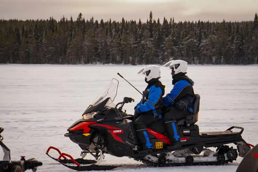 Group of six people posing cheerfully with snowmobile