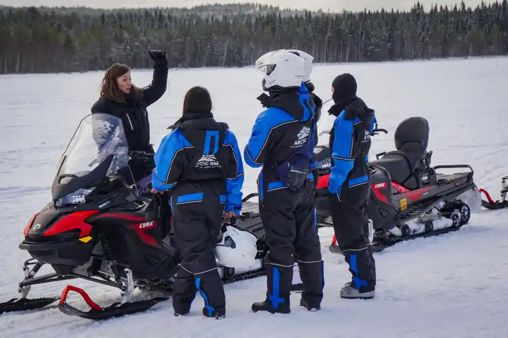 Guide instructing group near snowmobiles on frozen lake