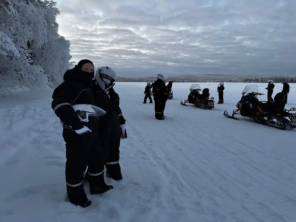 People on frozen lake with snowmobiles and cliff backdrop