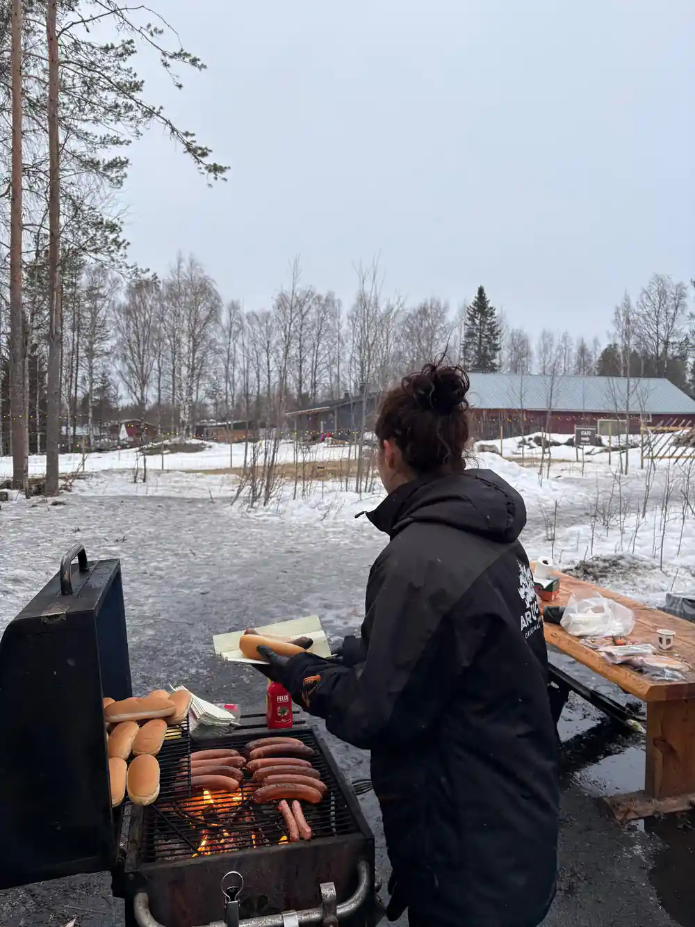 Person grilling food by frozen lake with trees