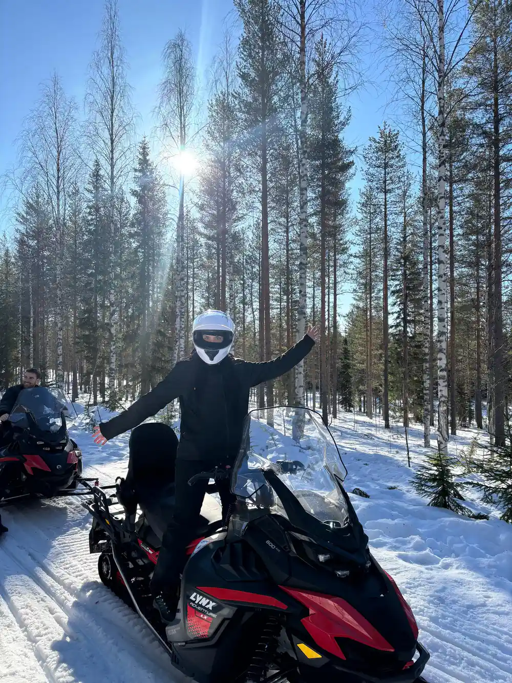 Person standing on snowmobile with arms raised on lake