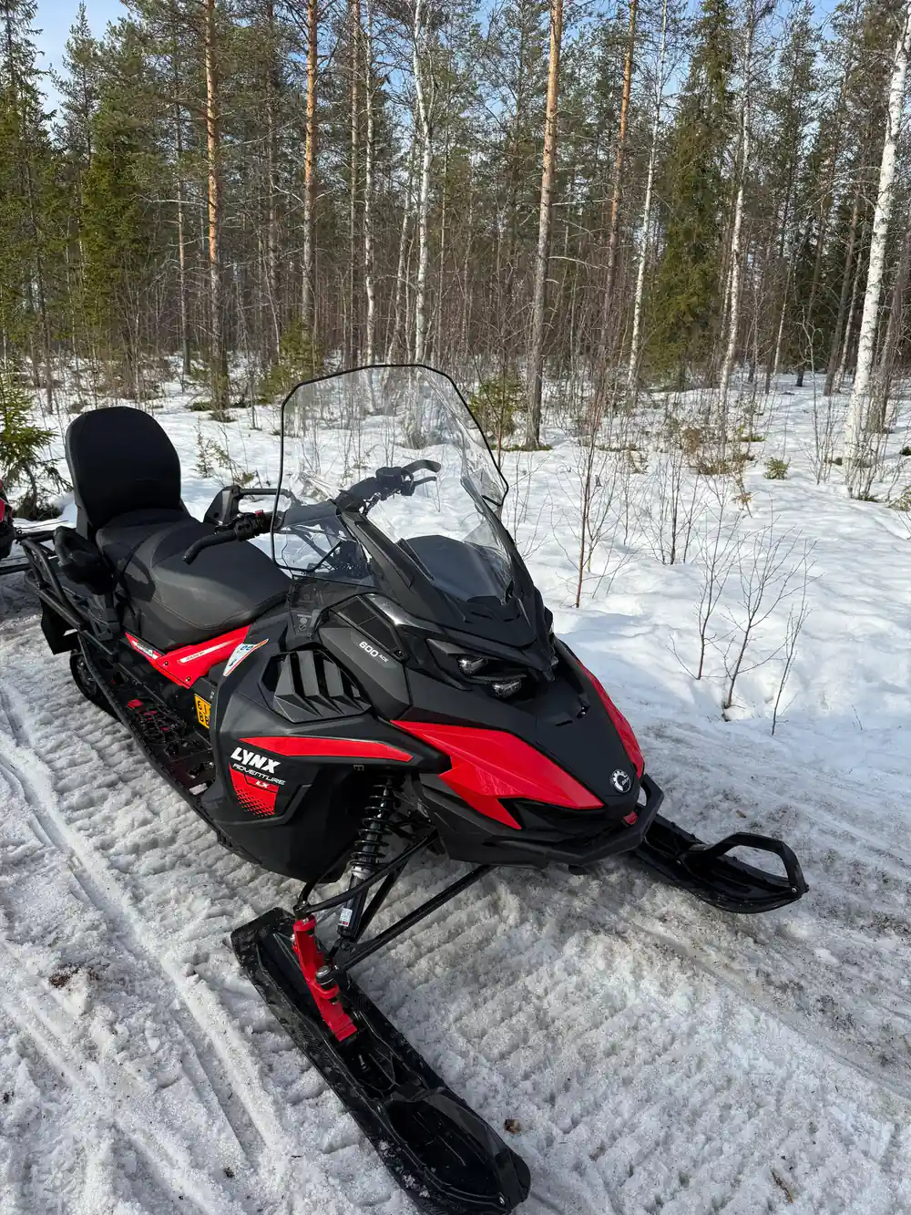 Red and black snowmobile parked on snow with forest behind