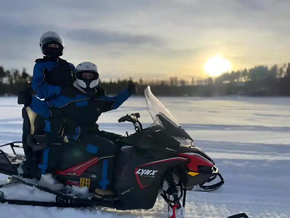 Two people riding snowmobile on frozen lake at dusk