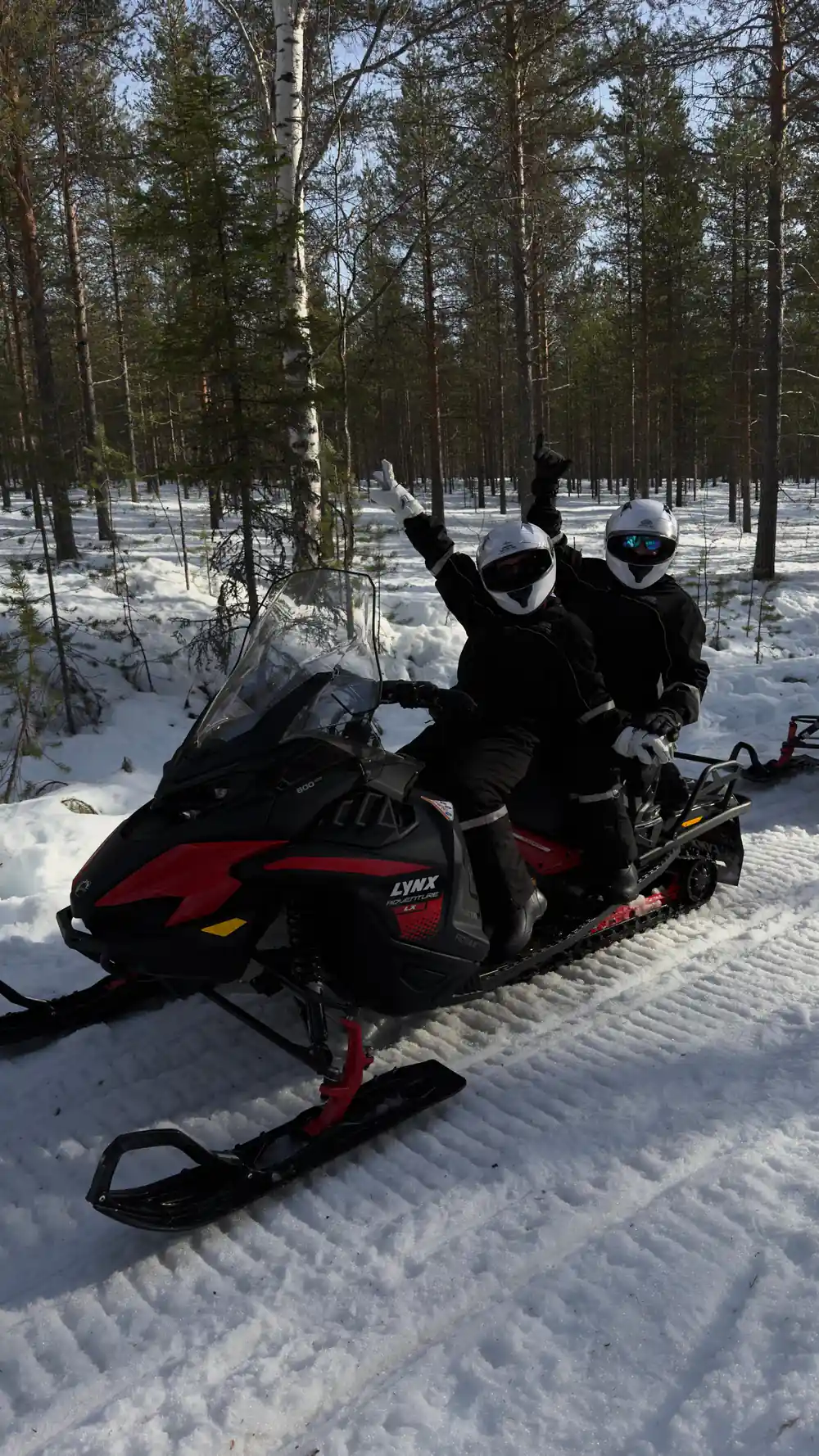 Two people on snowmobile in snowy forest clearing