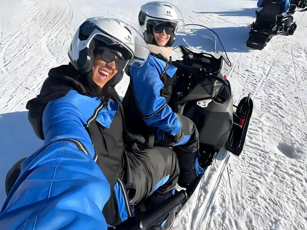 Two people in winter suits smiling near snowmobile