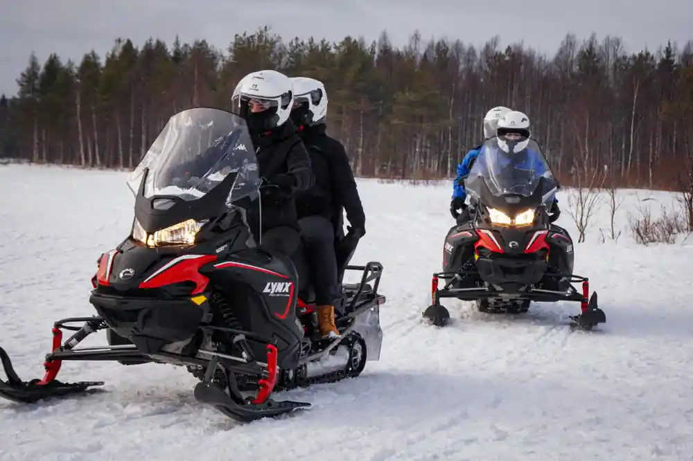 Two snowmobiles riding on frozen lake in winter landscape